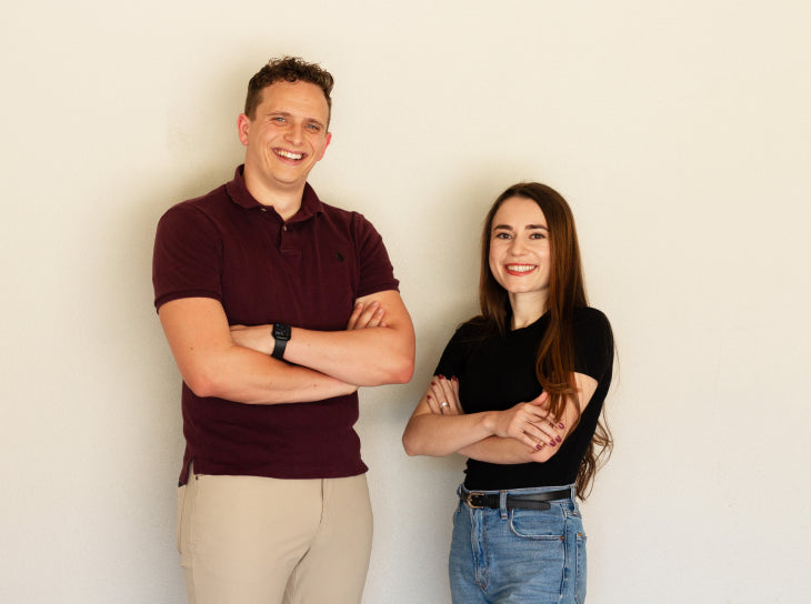 The Founders of UNDR, Carson and Mari, smiling with arms crossed against white wall