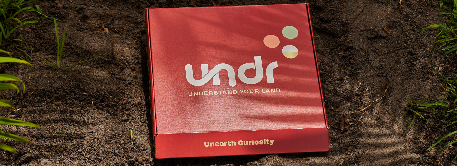 Red UNDR soil sample kit box on dirt, says 'Understand Your Land' and 'Unearth Curiosity'
