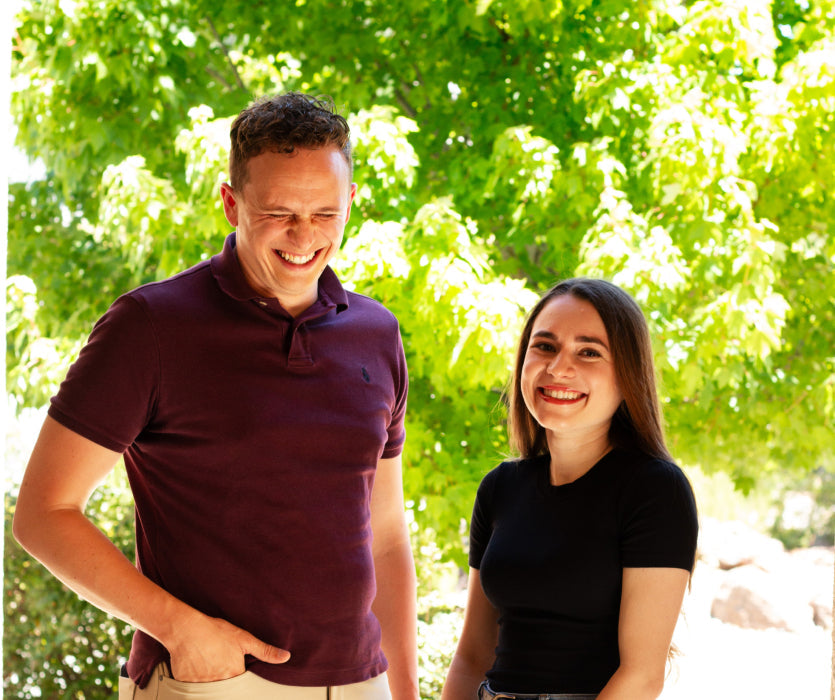 Man and woman smiling outdoors near green trees, enjoying time on their property