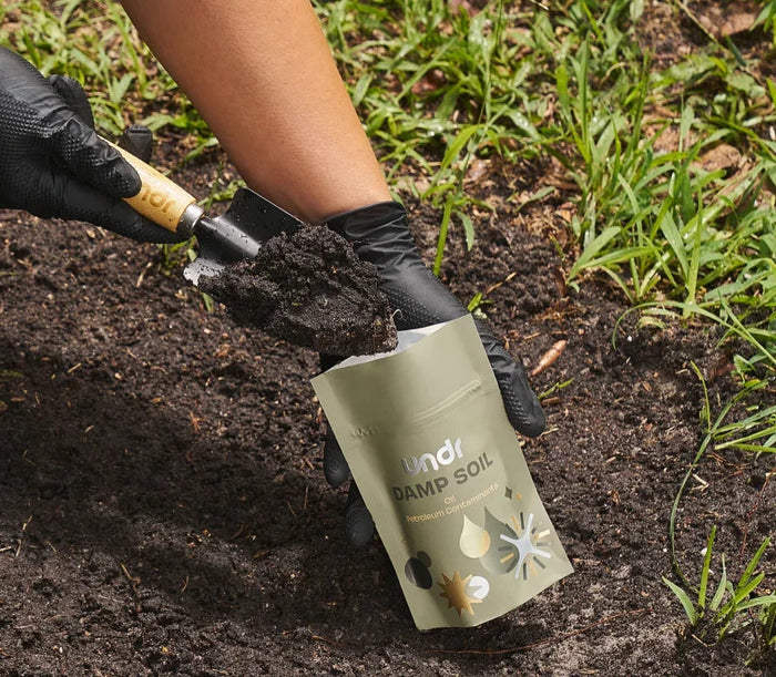 A shovel and a sample pouch on damp soil
