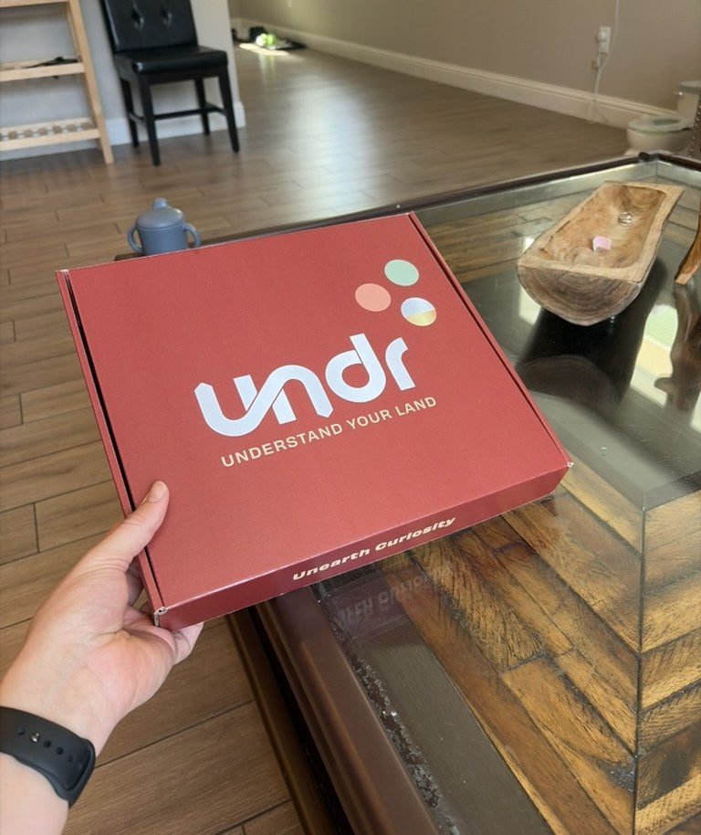 A hand holding the red UNDR kit box over a table at home