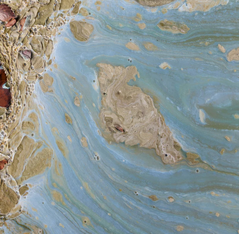 Soil sample in water showing swirls of blue, tan, and brown with small bubbles and leaf debris.